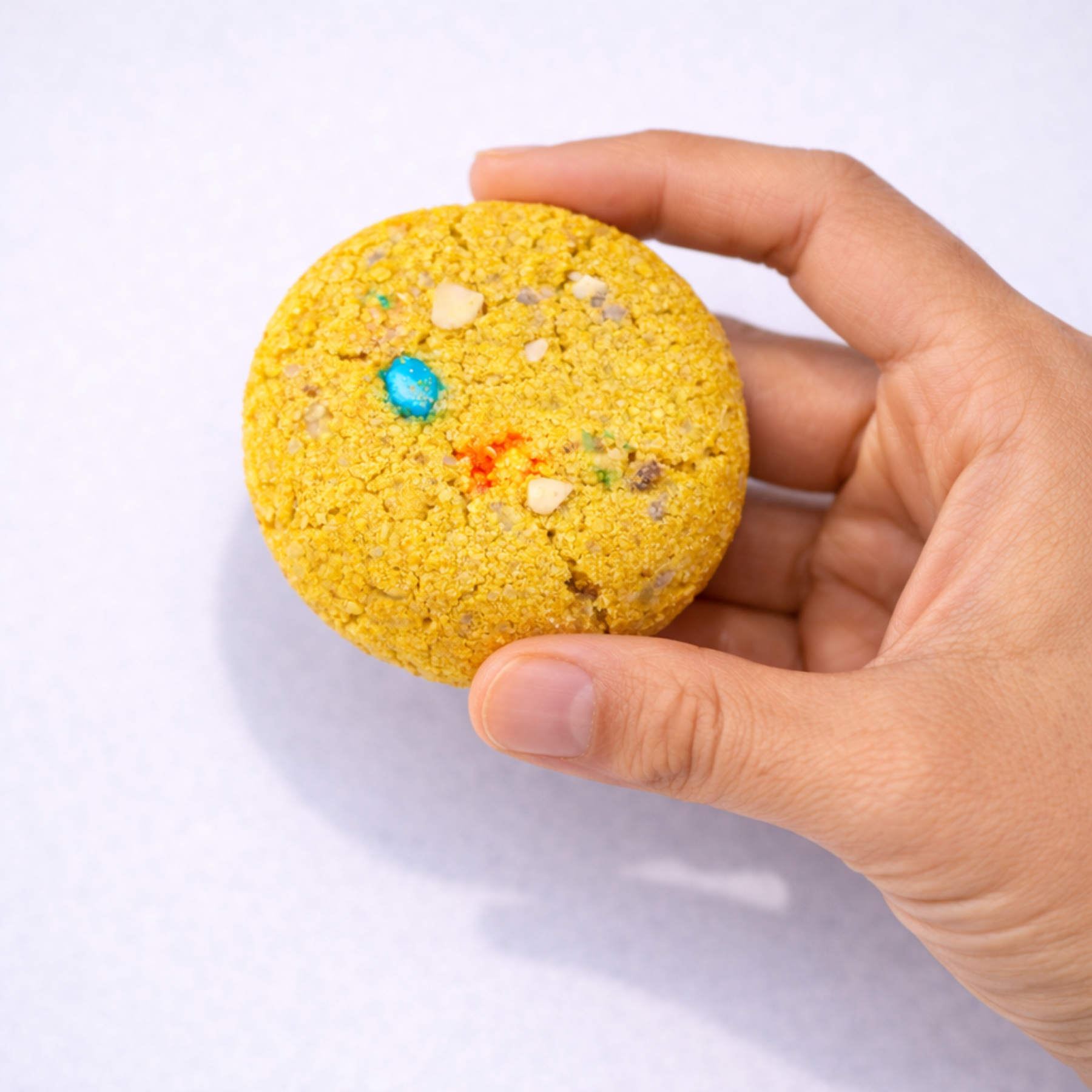 Hand holding a yellow cookie with colorful sprinkles on a white background