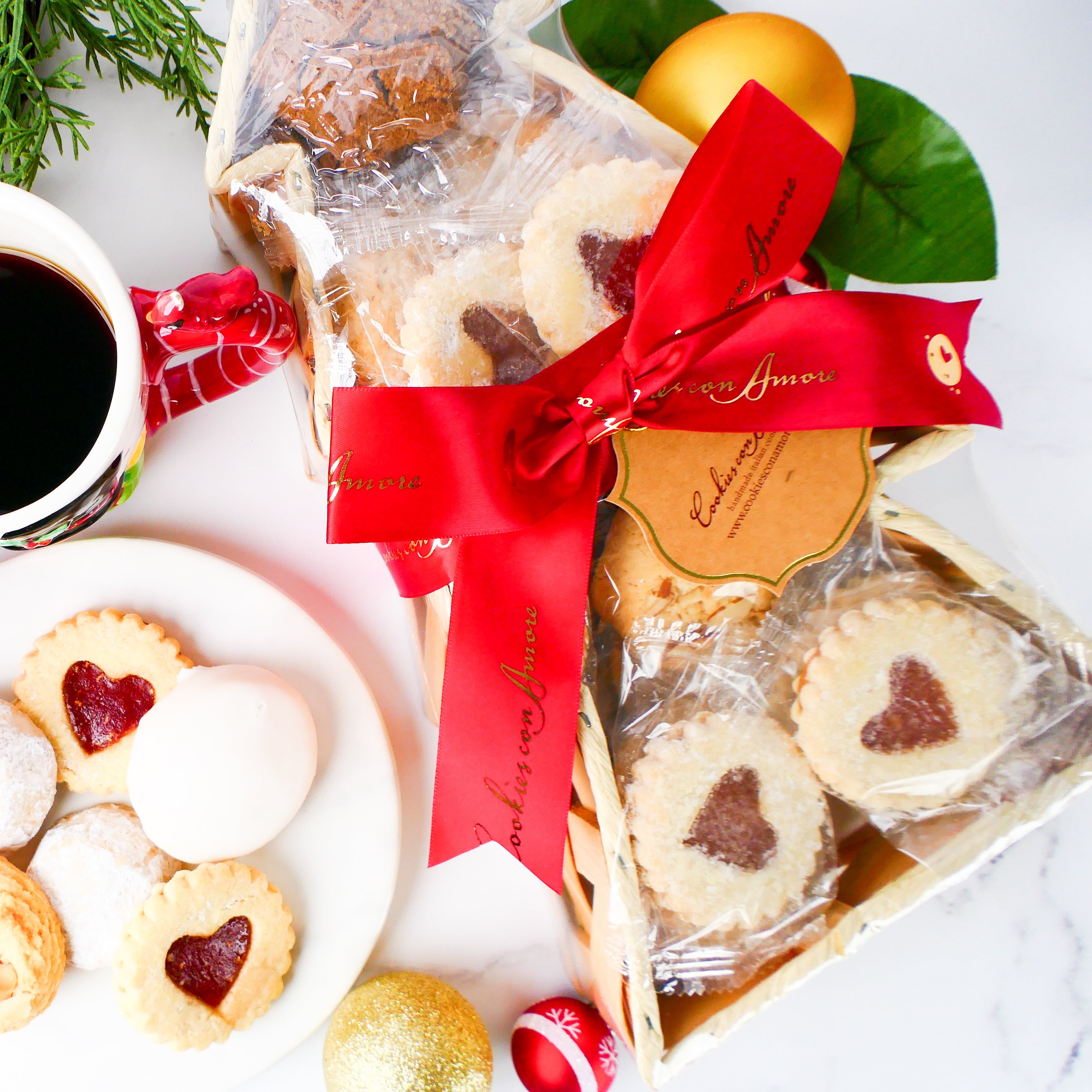 Packaged cookies with a red ribbon, coffee, and cookies on a white surface with greenery.