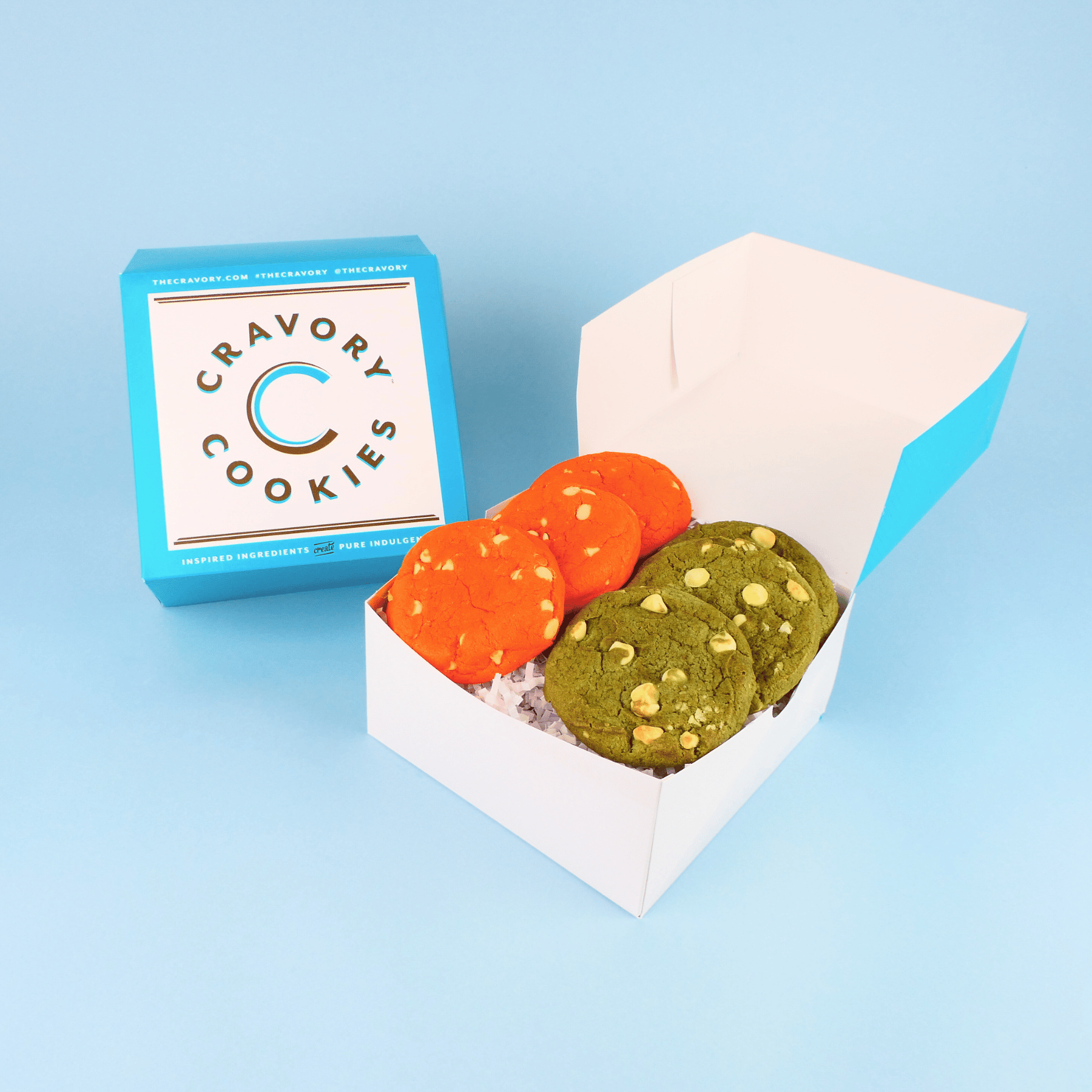 Open box of Cravory Cookies with two cookies, one orange and one green, on a blue background.