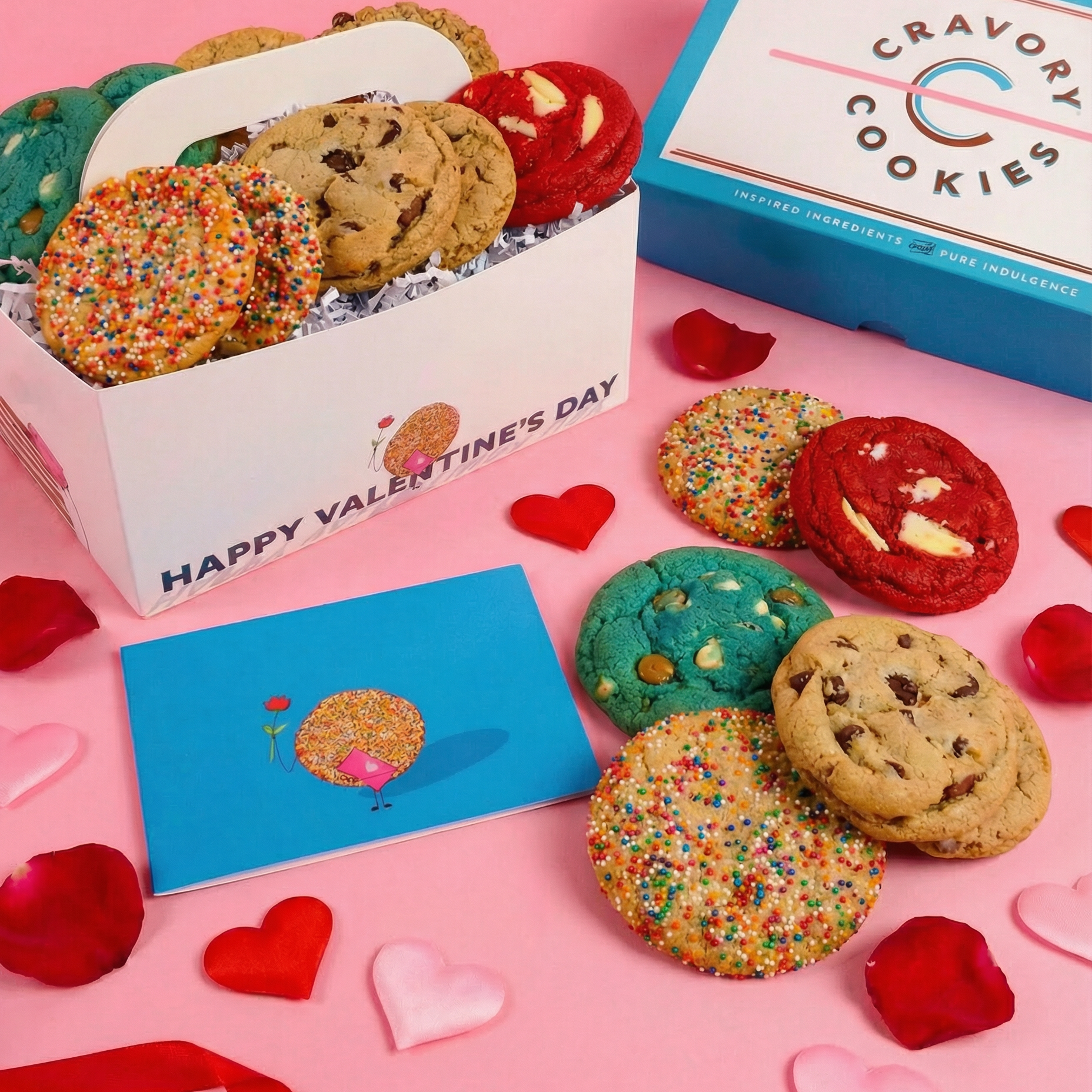 Box of Cravory Cookies with Valentine's Day cards and rose petals on a pink background