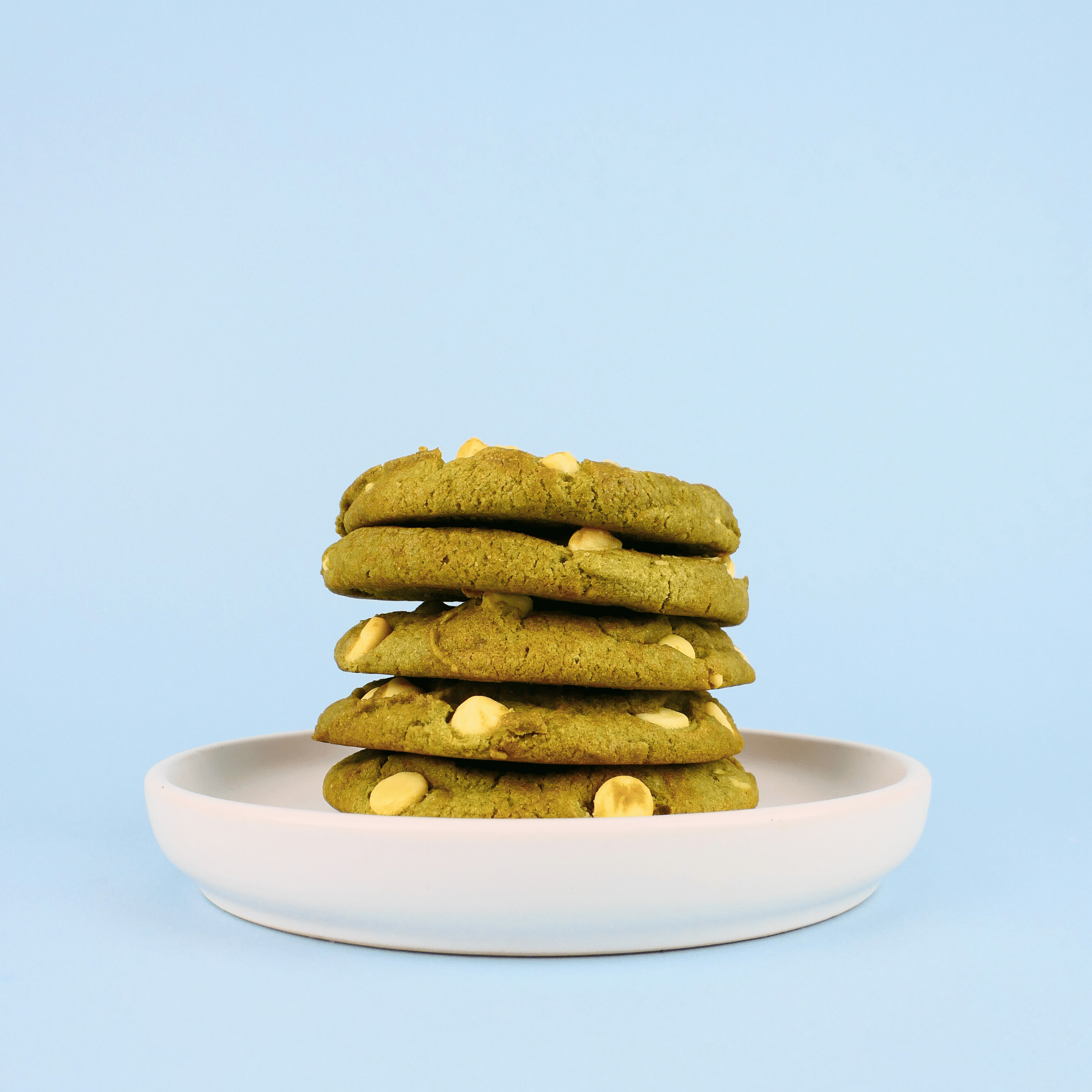 Stack of green cookies with white chips on a white plate against a light blue background