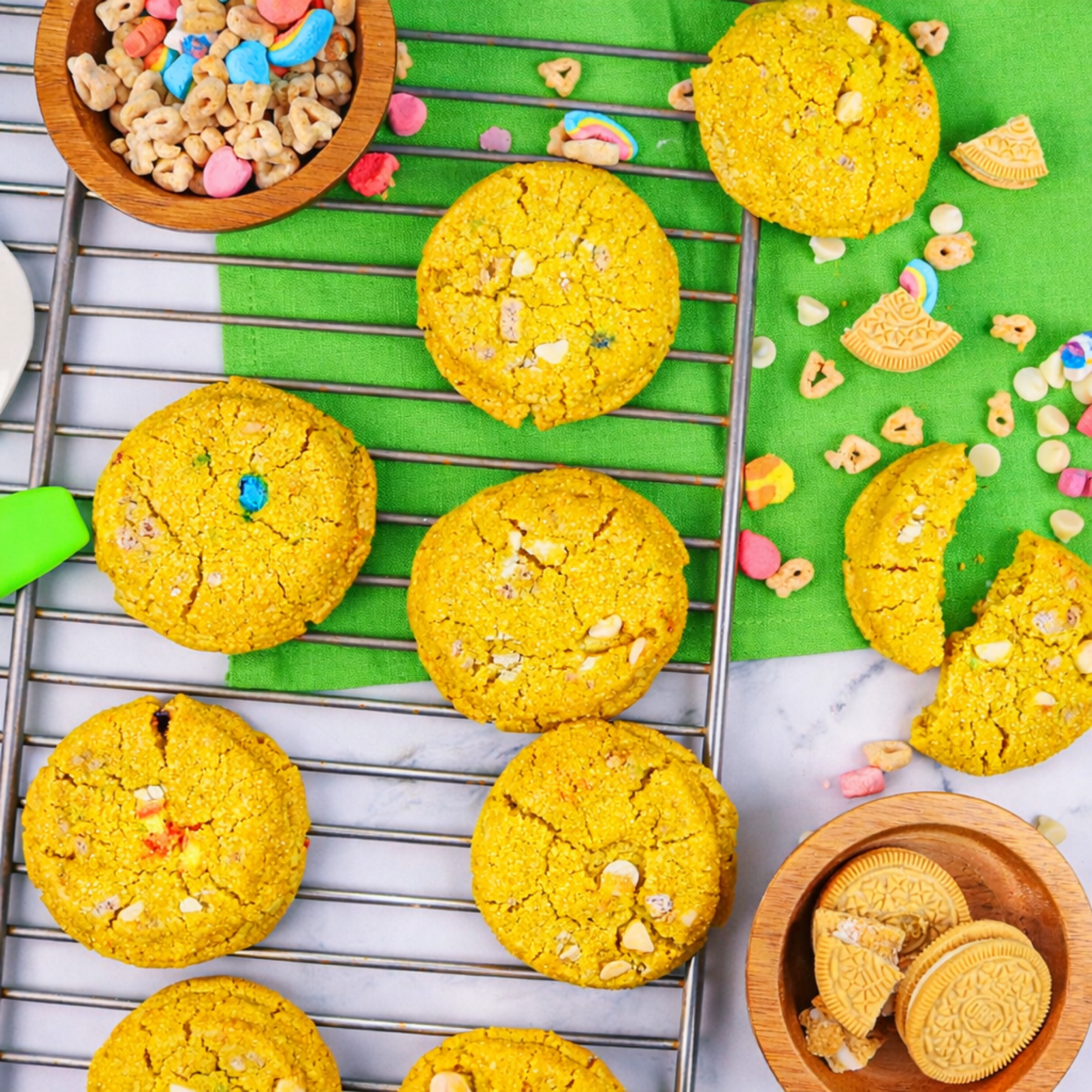 Yellow cookies on a cooling rack with colorful cereal pieces and cookies in wooden bowls.